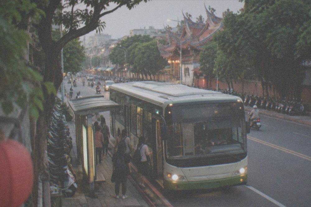 A Tainan city bus at a lit bus stop in the evening with passengers boarding