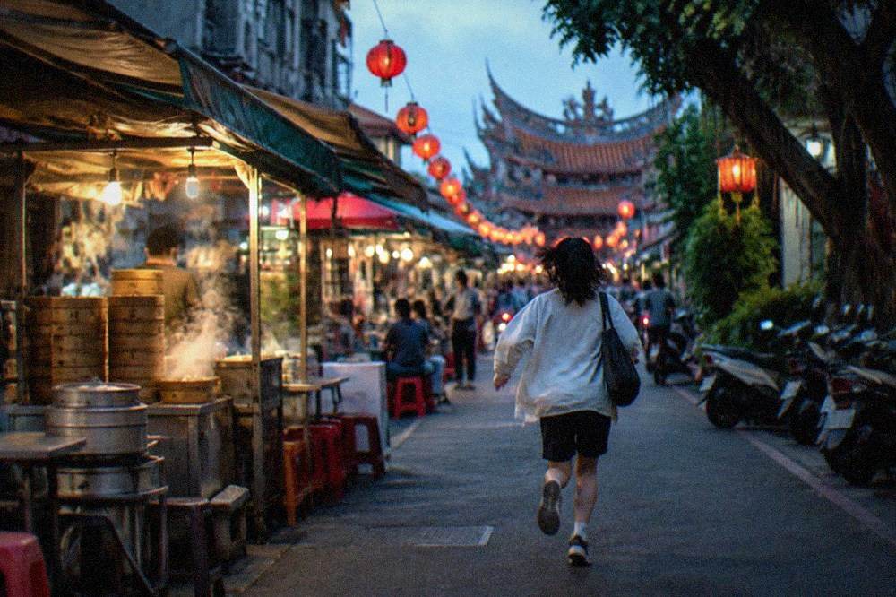 A narrow Tainan food street in the evening with crowded snack stalls and red lanterns overhead