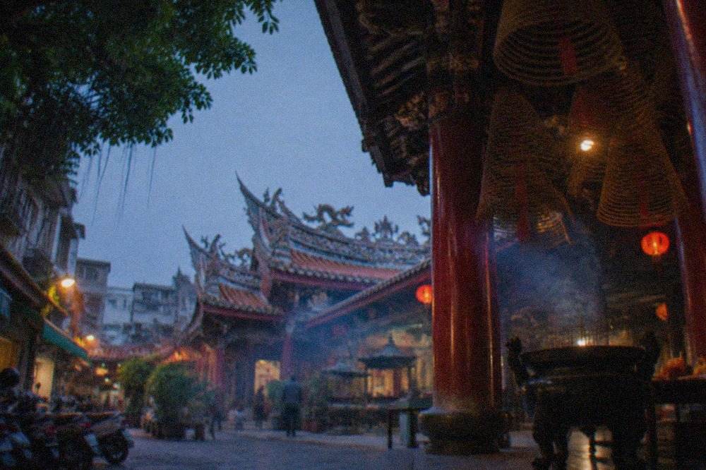 Courtyard of a Taiwanese temple with red walls, ornate tiled roof and incense smoke drifting in daylight