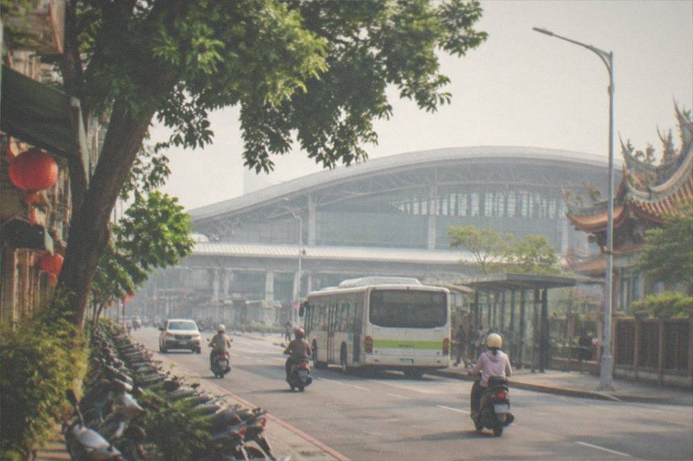 A city bus parked at a station curb outside a rail terminal