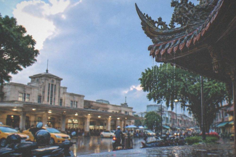 Rain dripping from the eaves of a traditional temple roof in Tainan, carved decorations visible along the roofline