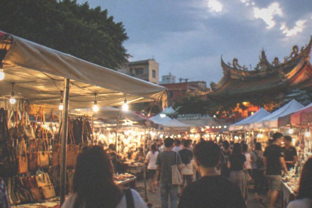 Crowded night market stalls lit by strings of bulbs