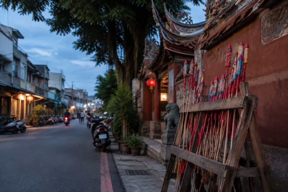A wooden rack of firecracker rockets waiting to be lit beside a temple wall
